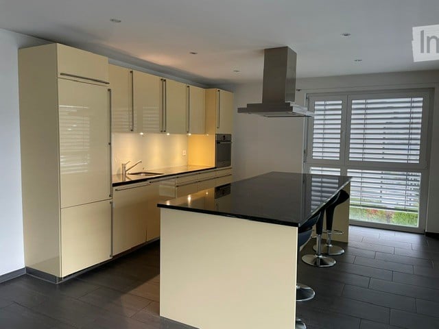 Modern kitchen with light-colored cabinets, stainless steel appliances, and a black countertop island with bar stools.