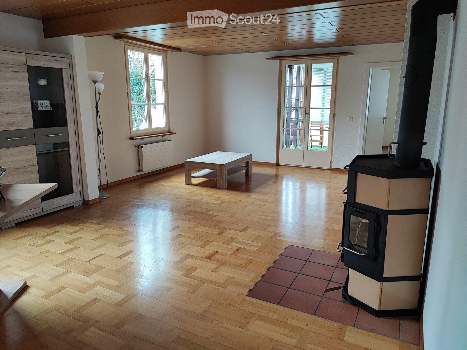 Bright living room with wooden flooring, fireplace, table, floor lamp, and cabinet.