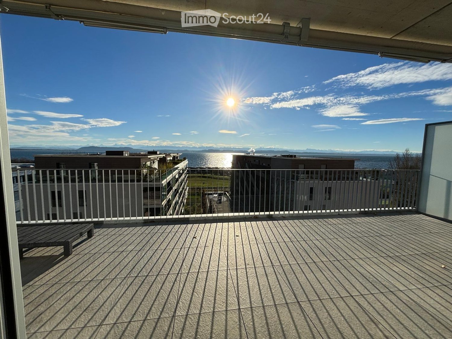 Balcony with wooden decking, metal railing, bench, and scenic view of water and distant mountains.