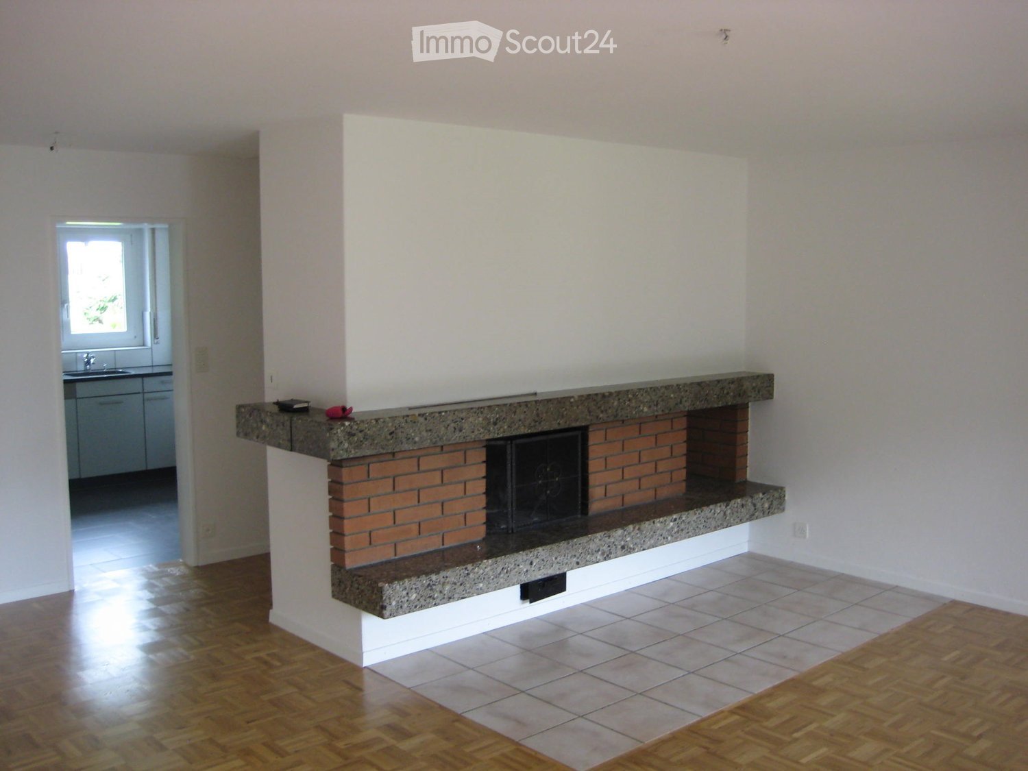 Empty room with a fireplace, wooden flooring, and tiled area near the fireplace.