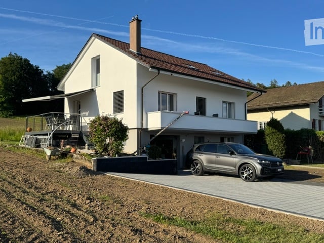 Two-story house with white exterior, brown roof, garage, and parking area.