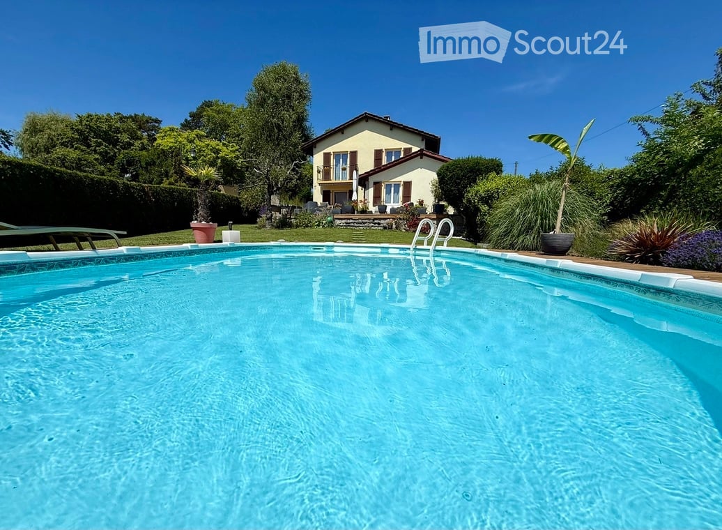 A private swimming pool in a well-maintained garden area with a house in the background, surrounded by greenery and potted plants.