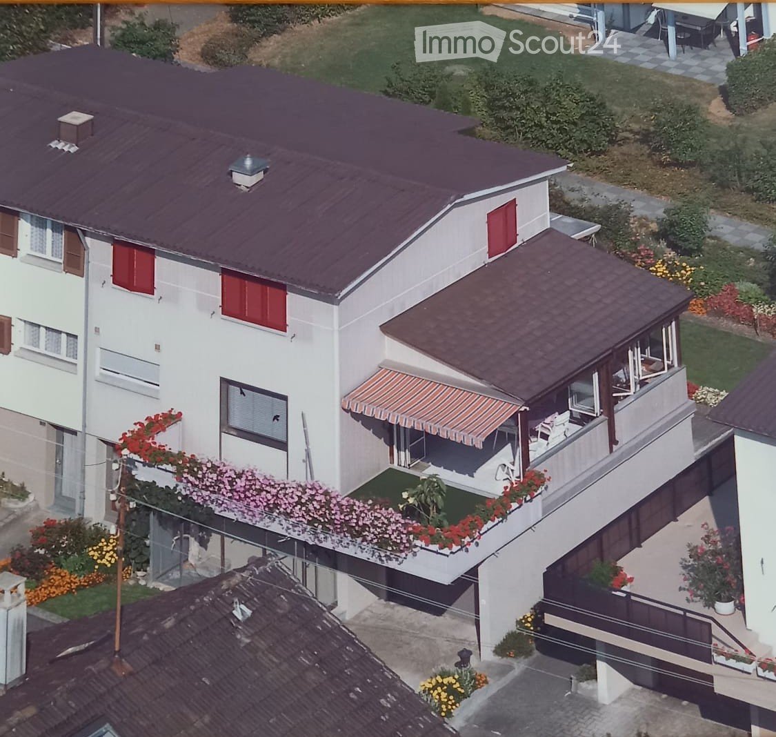 Two-story house with red shutters, a balcony with flower boxes, and a covered patio area with outdoor furniture.
