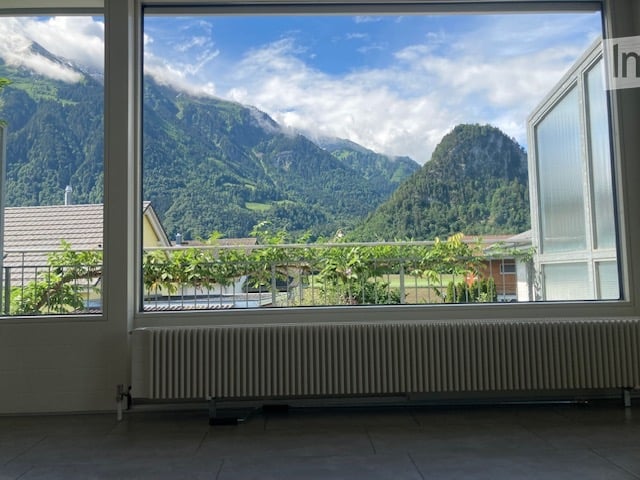 Empty room with large windows offering a scenic mountain view, radiator below the windows, and a metal railing outside.