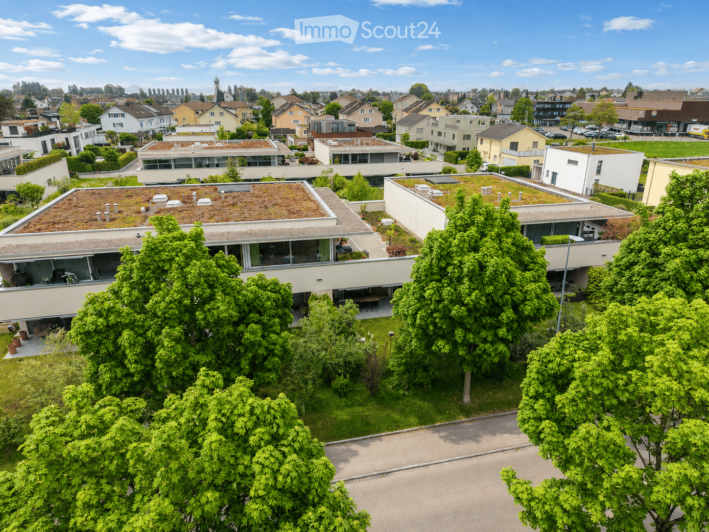 Aerial view of a modern residential complex with multiple buildings, green roofs, and surrounding greenery.
