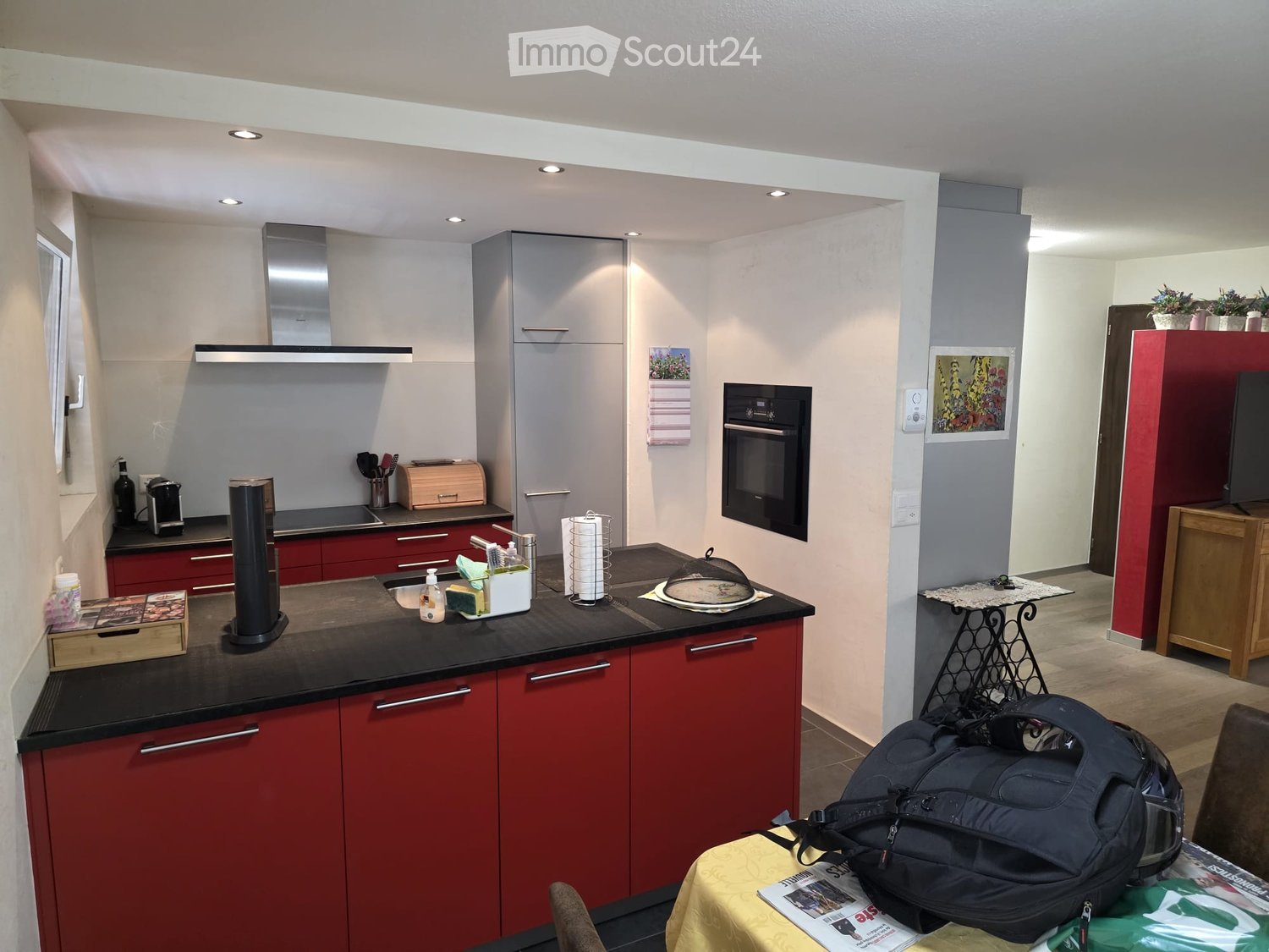 Modern kitchen with red cabinets, black countertops, stainless steel appliances, and a small dining area with a table and chair.