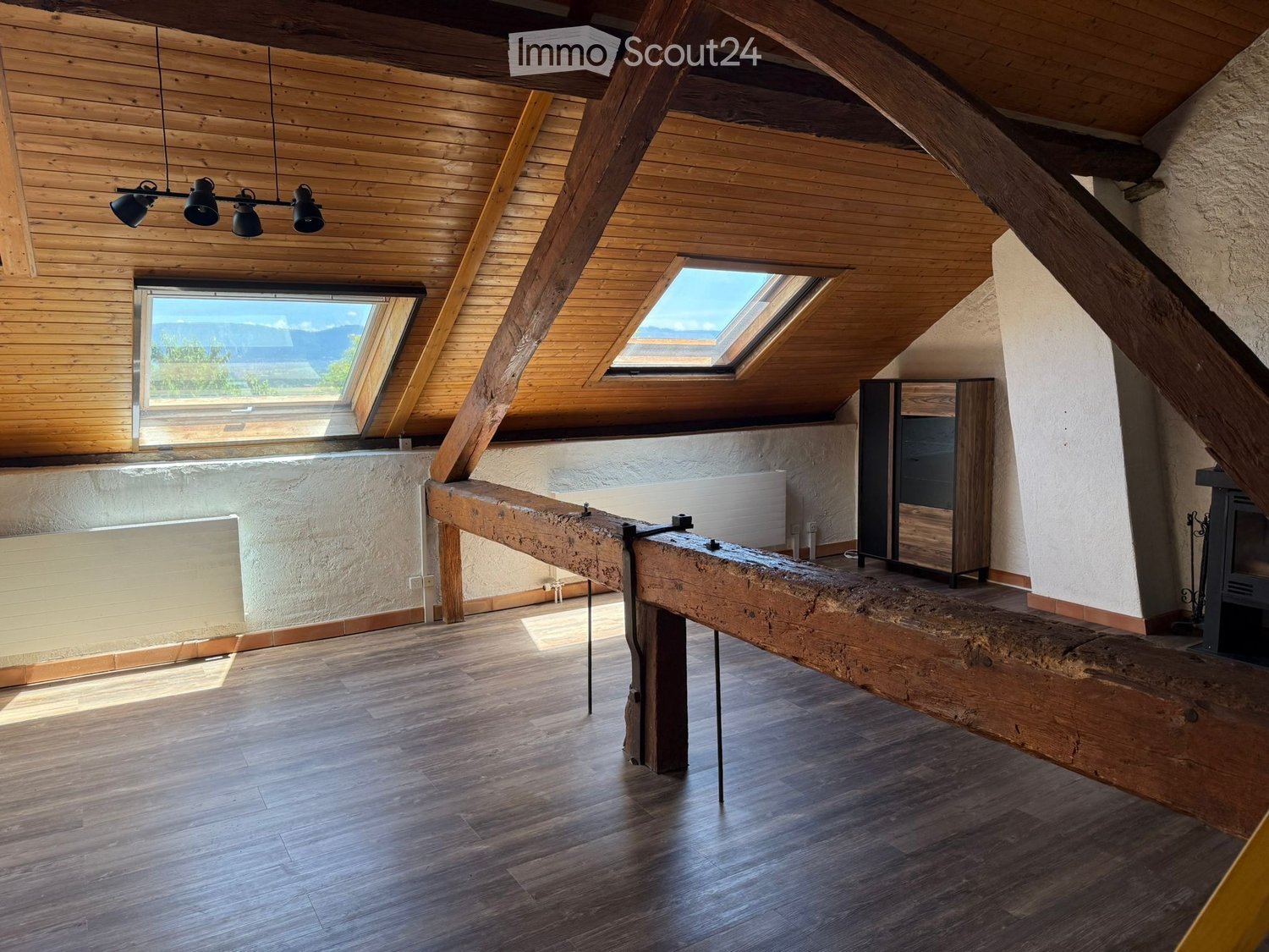 Loft-style room with wooden beams, skylights, a long wooden table, a cabinet, and a fireplace.