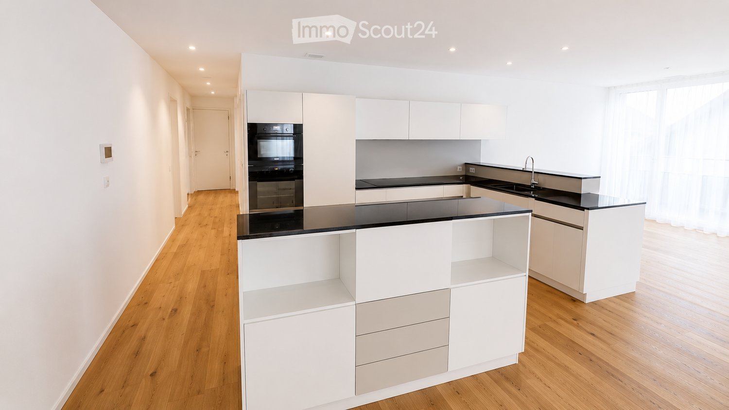Modern kitchen with white cabinets, black countertops, and a central island. Features include an oven, sink, and faucet.