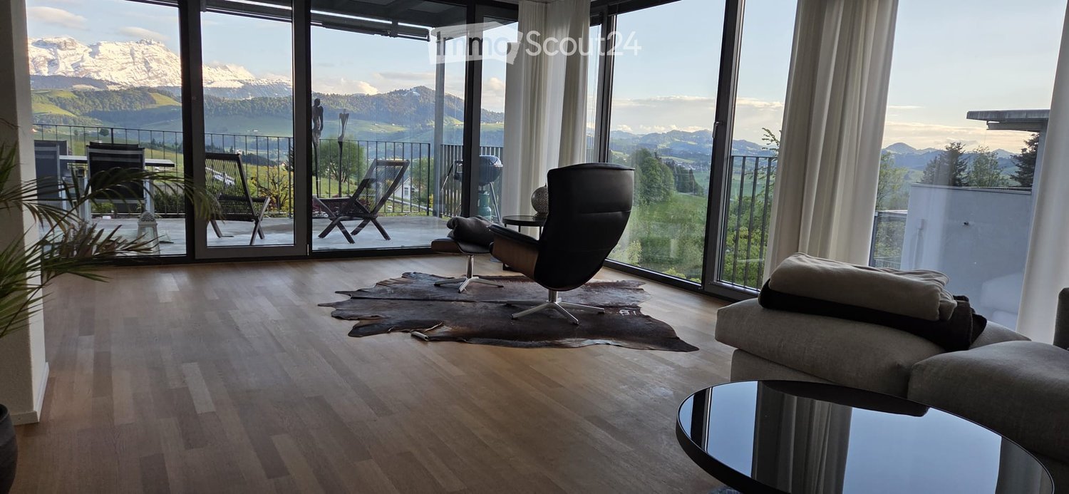 Furnished Room. Modern living room with large windows offering a scenic mountain view, featuring a sofa, chairs, coffee table, and a small table on the balcony.