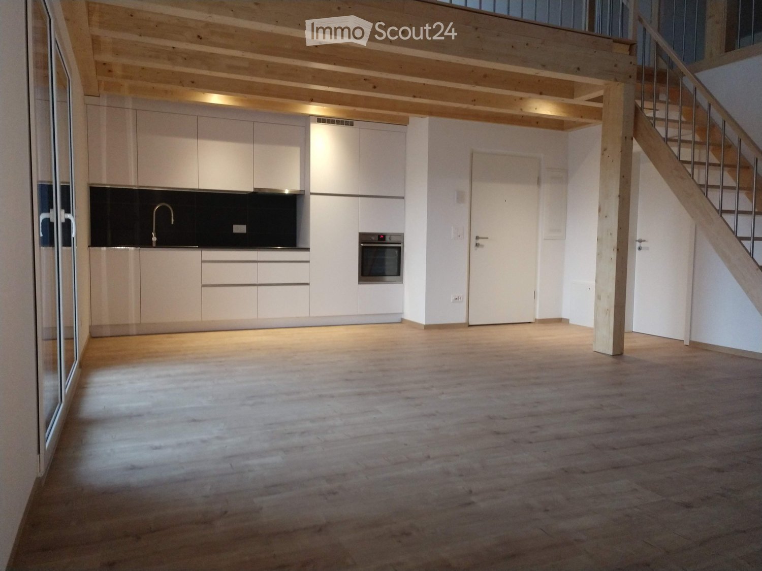 Modern kitchen with white cabinets, a sink, and an oven, featuring wooden flooring and exposed wooden beams on the ceiling.