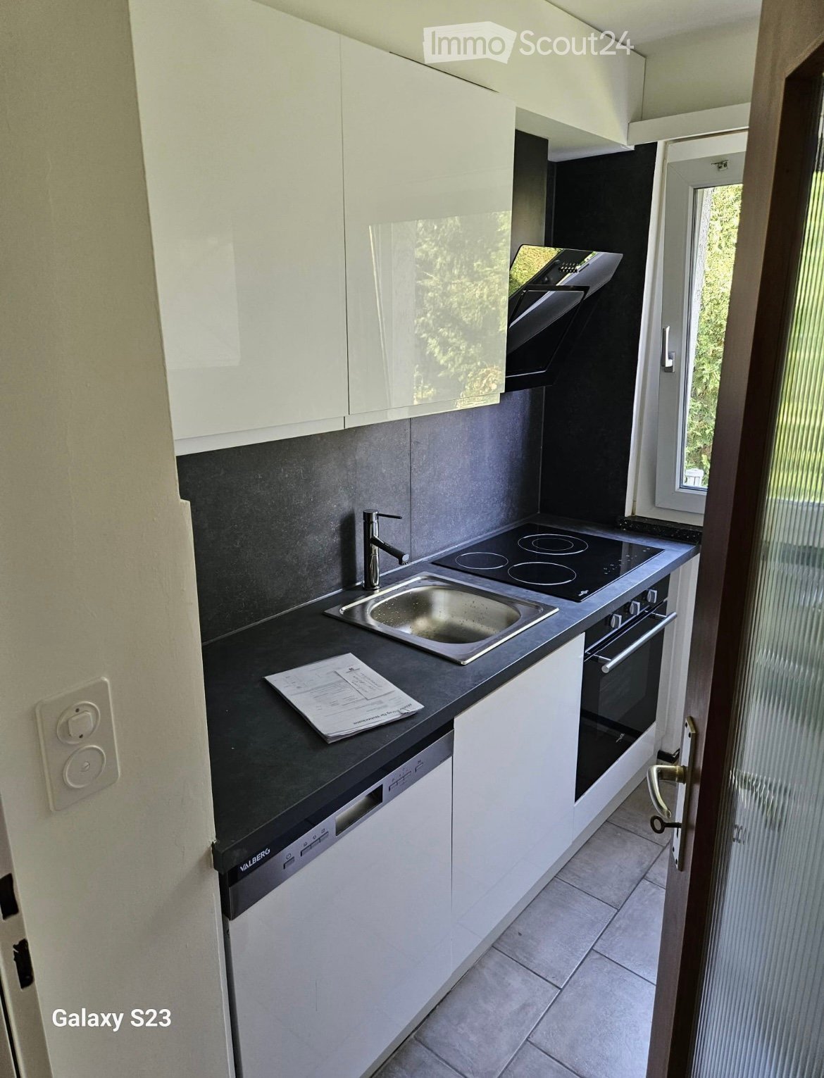Modern kitchen with white cabinets, black countertops, stainless steel sink, and built-in appliances including an oven and dishwasher.