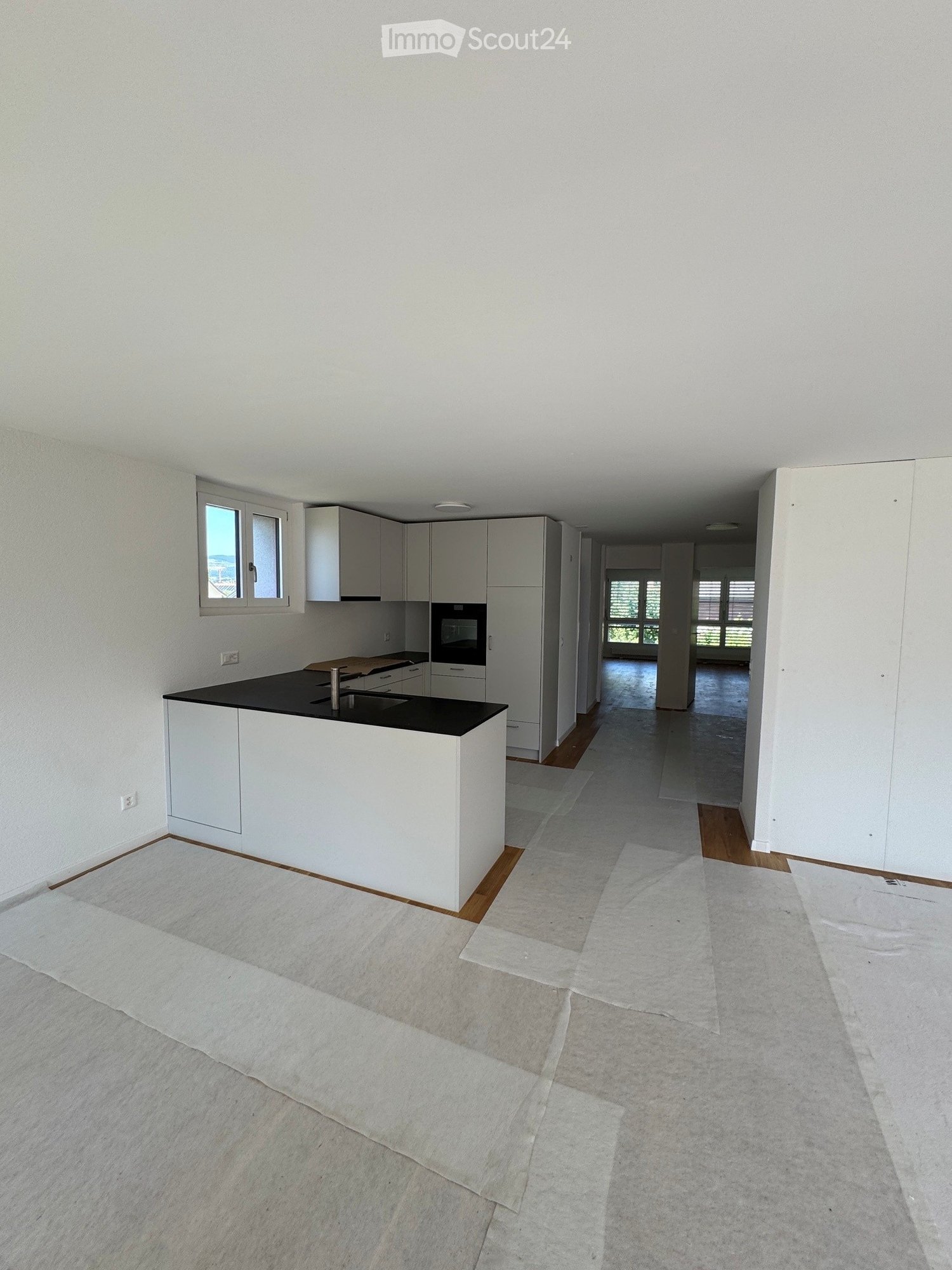 Empty kitchen and hallway area with white cabinets, a black countertop, and a window. The floor is covered with protective sheets.