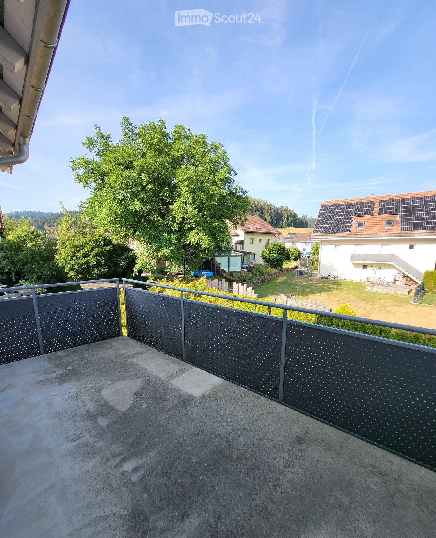 Balcony with metal railing overlooking a residential area with houses, trees, and a clear sky.