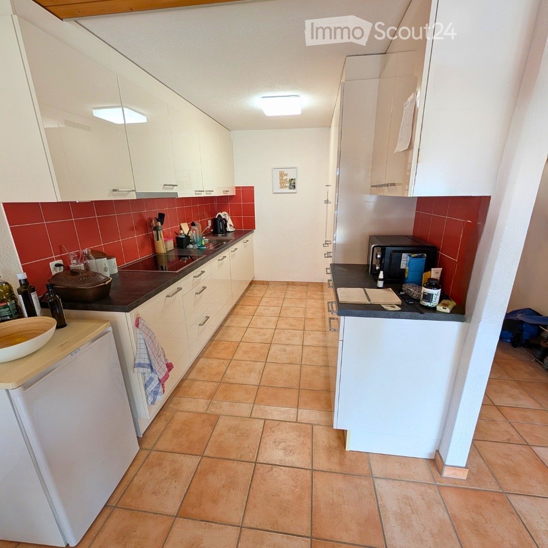 Modern kitchen with white cabinets, red tiled backsplash, and tiled floor. Features a refrigerator, microwave, oven, countertop, and various kitchen items.