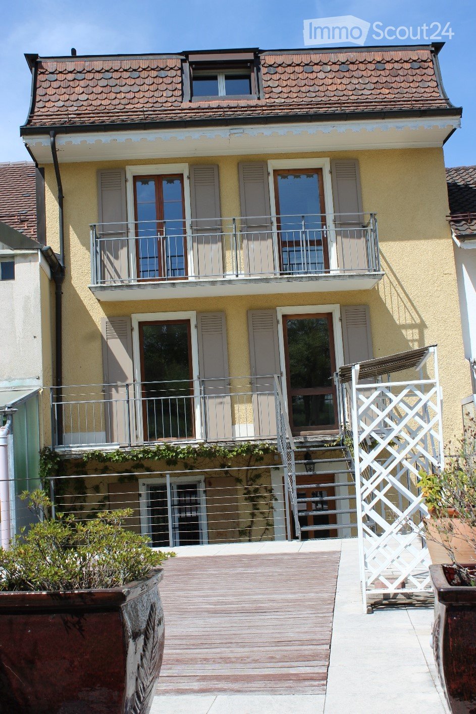 Two-story residential building with a balcony, wooden deck, and stairs leading to the entrance.