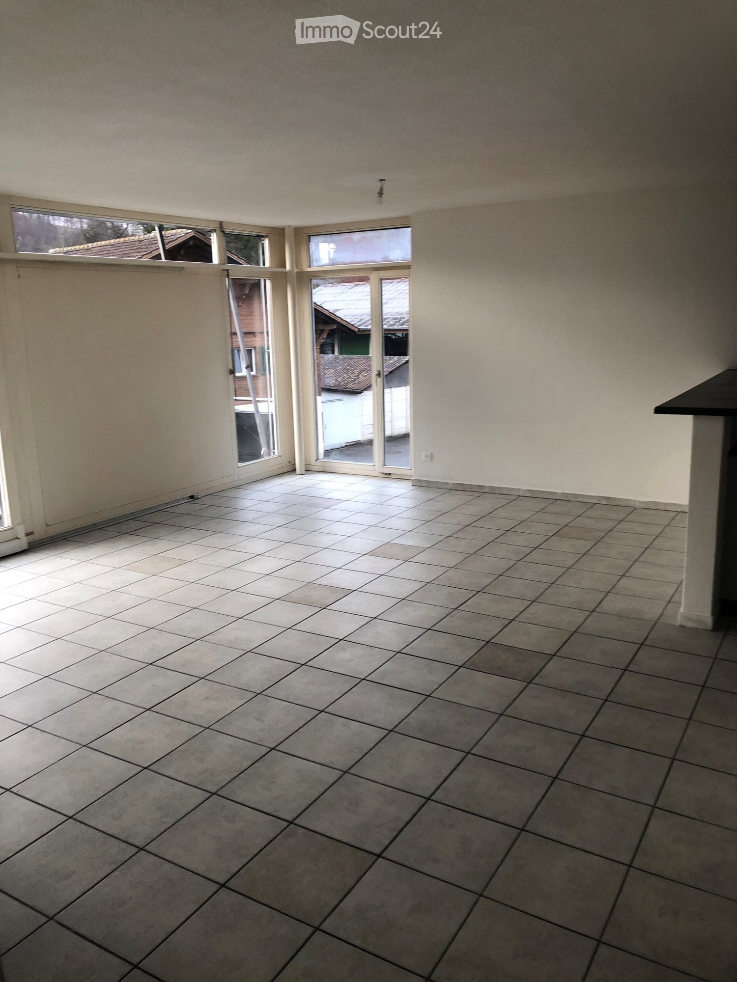 Empty room with tiled floor and large windows, featuring a sliding glass door leading outside.