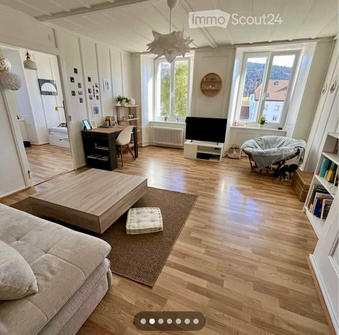 Bright living room with wooden flooring, large windows, a sofa, coffee table, desk, and a TV stand.