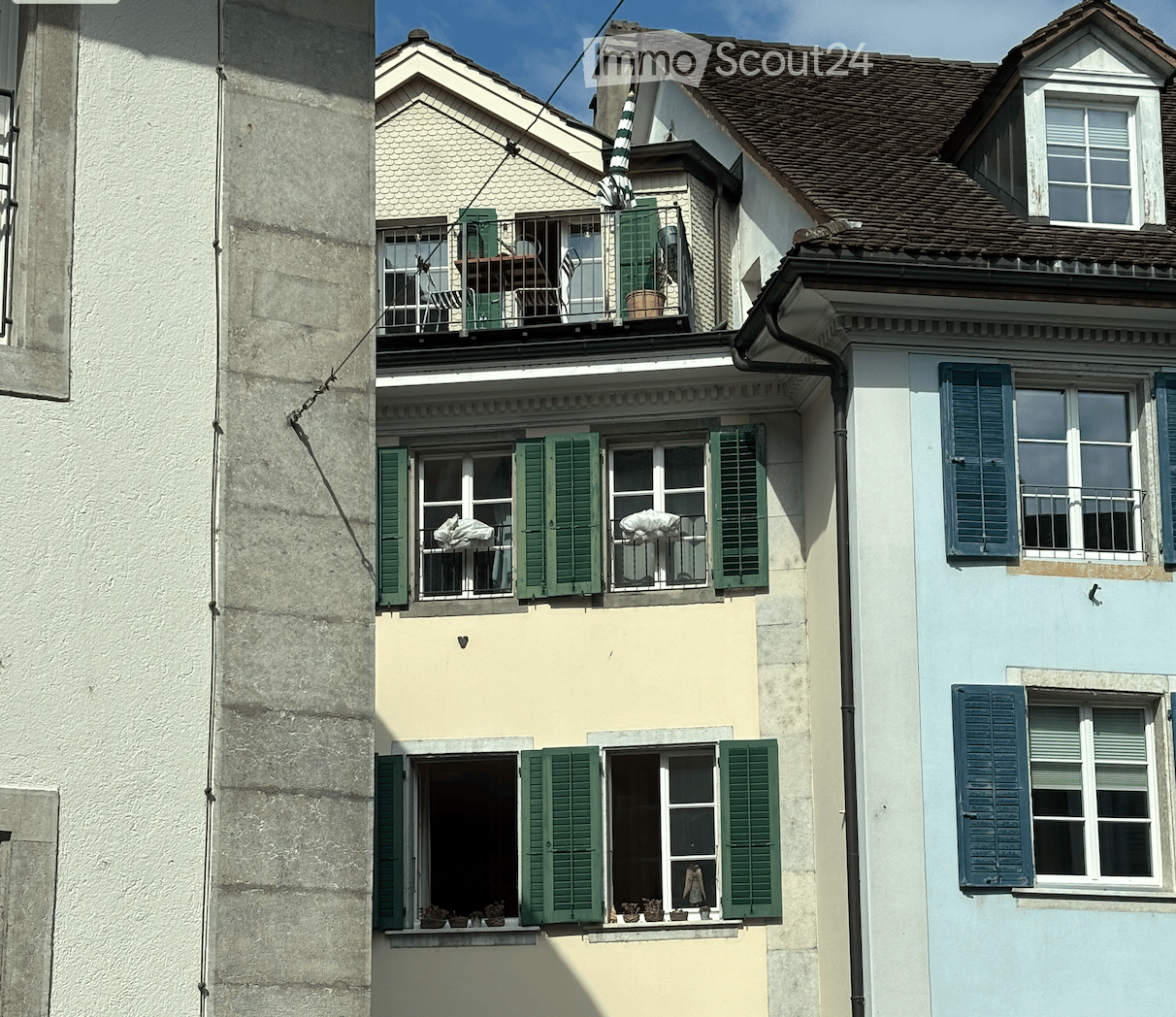 Multi-story building with green shutters, balconies, and potted plants on the windowsills.