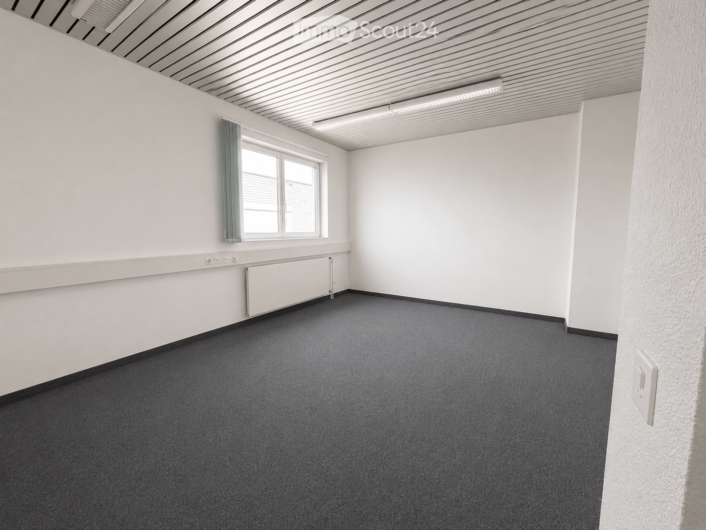 Empty room with white walls, grey carpet, a window with a green curtain, and a radiator below the window.