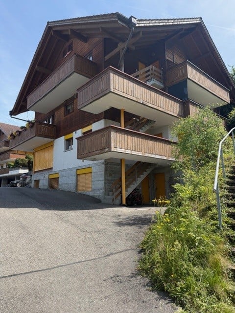A multi-story wooden chalet with balconies, large windows, and a gravel driveway.