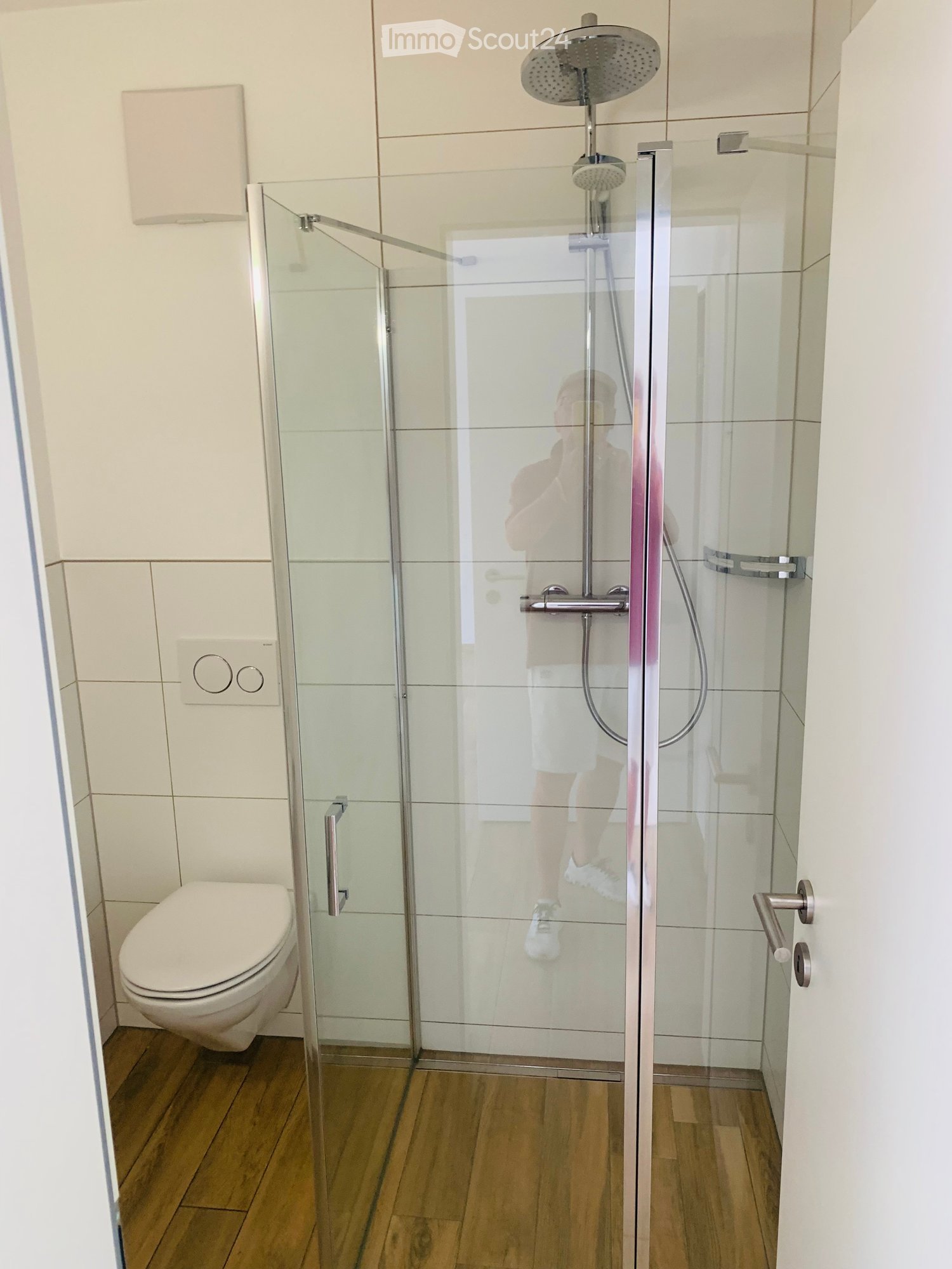 modern bathroom with walk-in shower, white toilet, white wall tiles, wooden floor