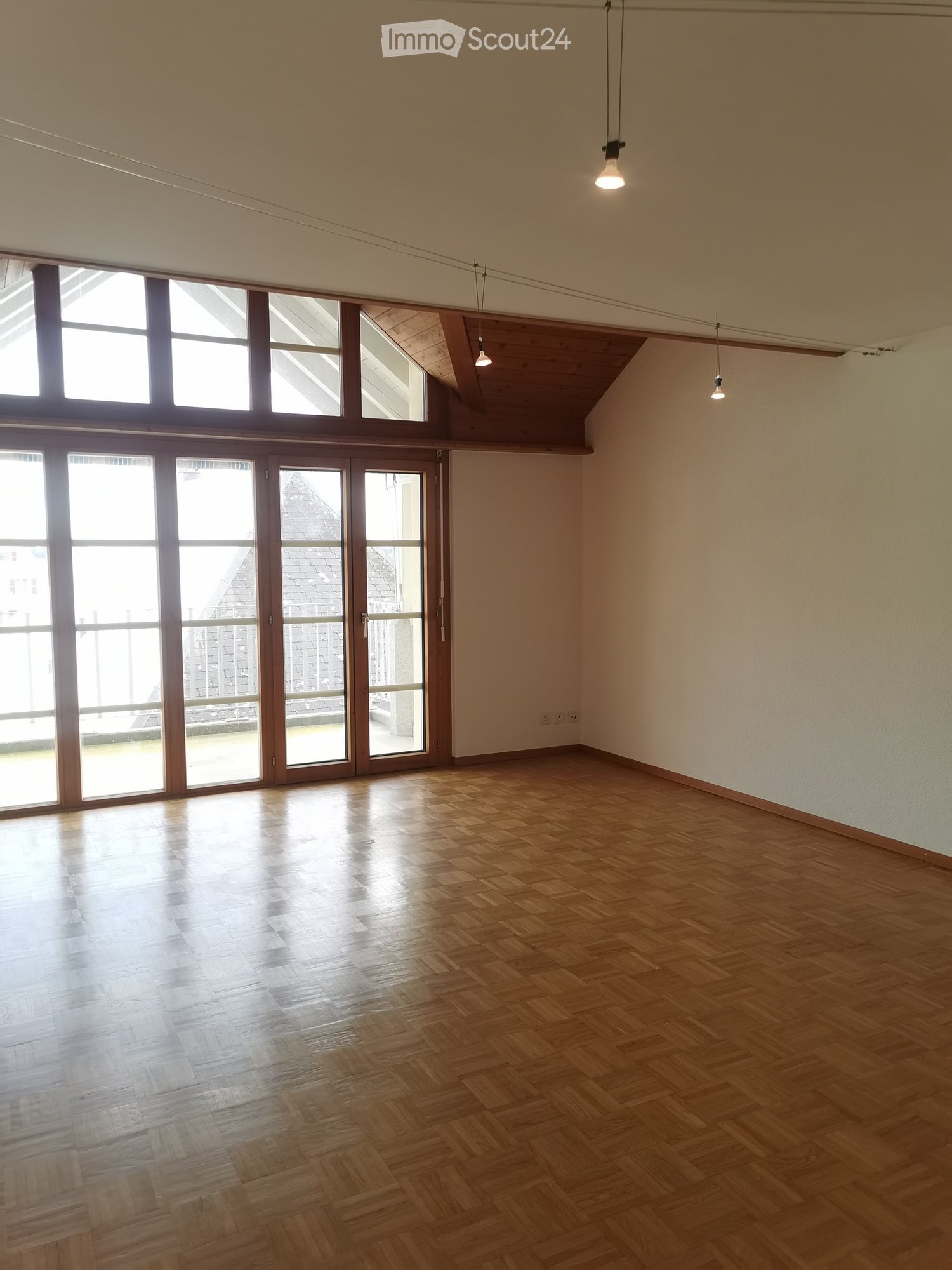 Empty room with wooden flooring, large windows, and skylights, featuring exposed wooden beams on the ceiling and pendant lights.