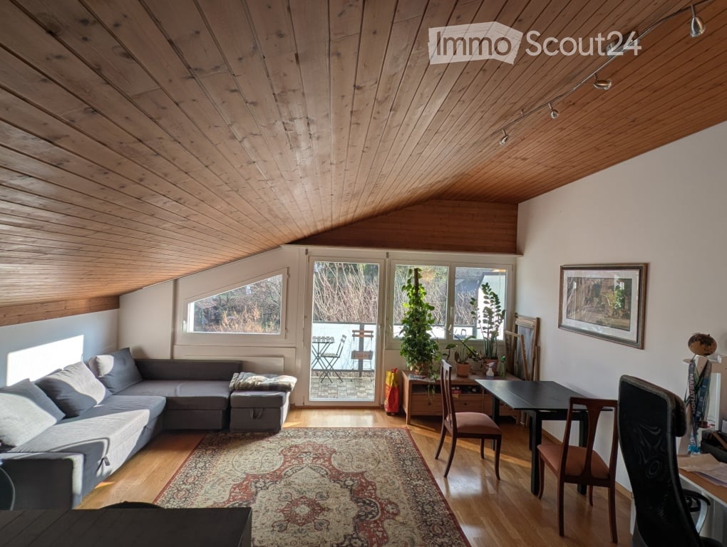 Living room with wooden ceiling, large windows, balcony access, sofa, coffee table, dining table, chairs, and plants.