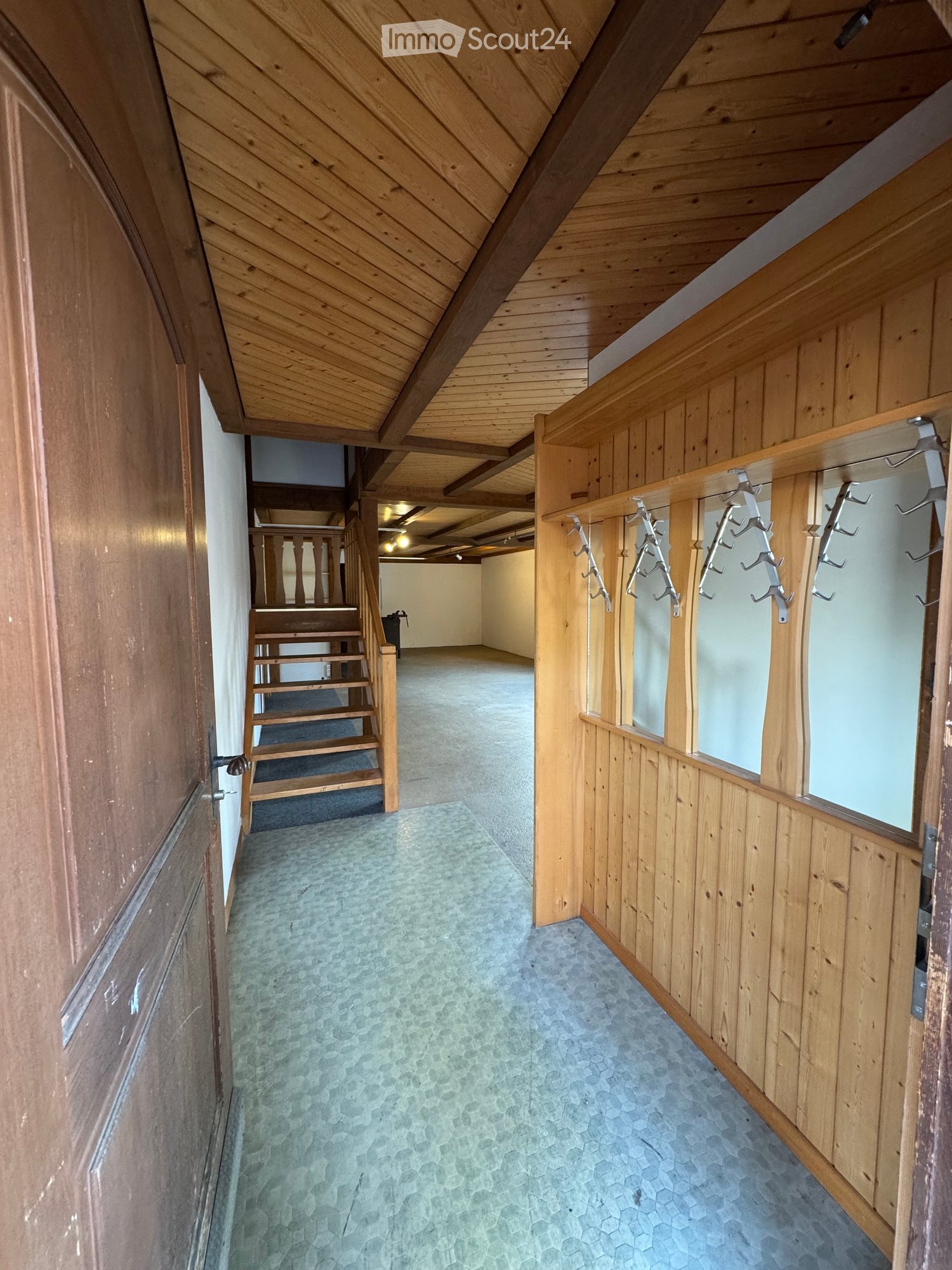 A wooden-paneled hallway with a staircase leading upwards, featuring a coat rack with hooks on the right side and a carpeted floor.