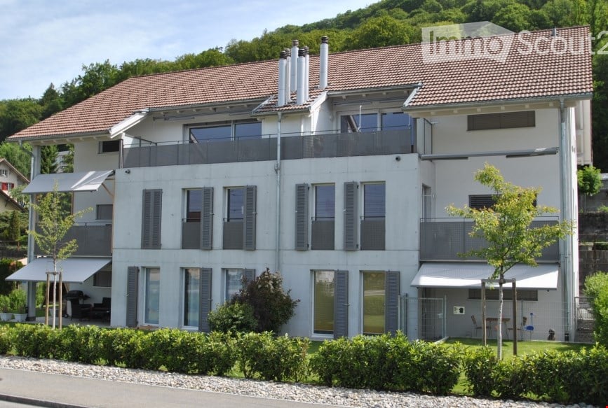 Modern two-story house with white facade, large windows, multiple balconies, and a well-maintained garden.
