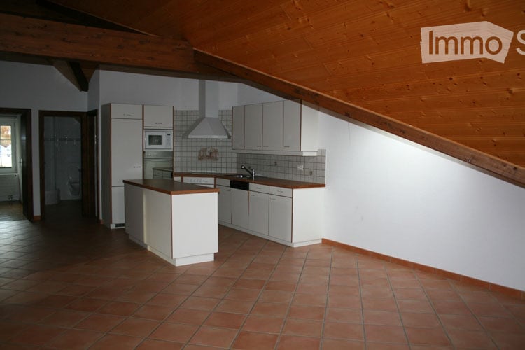 Bright kitchen with white cabinets, a refrigerator, microwave, and a sink. The space features a wooden slanted ceiling and terracotta tiled flooring.