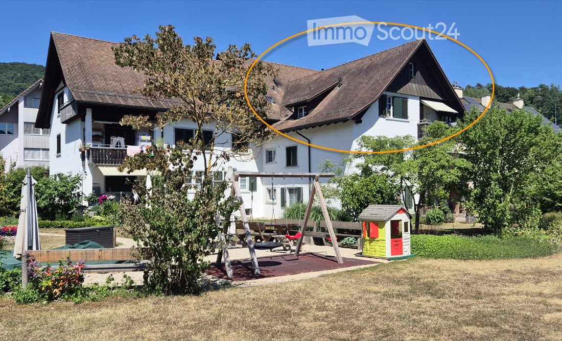 A two-story house with a brown roof and white walls, surrounded by a well-maintained garden with a swing set, a small playhouse, and a patio area.