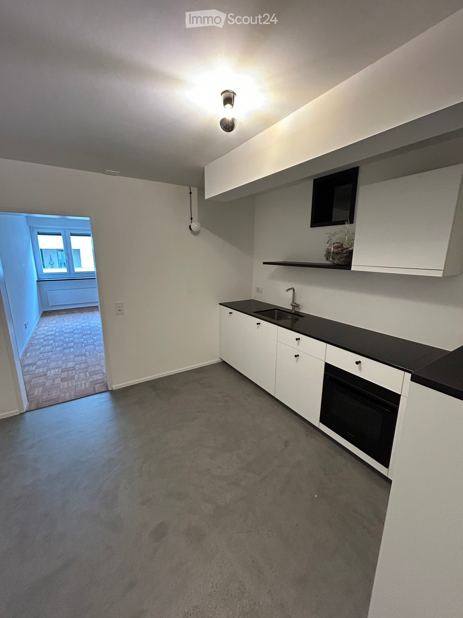 Modern kitchen with white cabinets, black countertop, sink, and oven. Open doorway leads to another room with brick flooring.