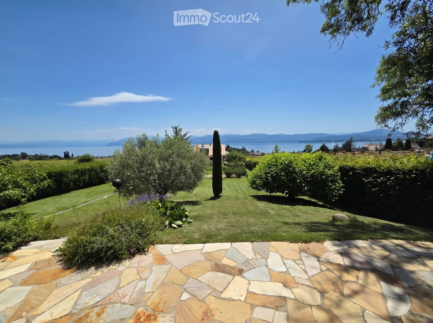Well-maintained garden with a stone pathway, neatly trimmed hedges, and a scenic view of a lake and distant mountains.