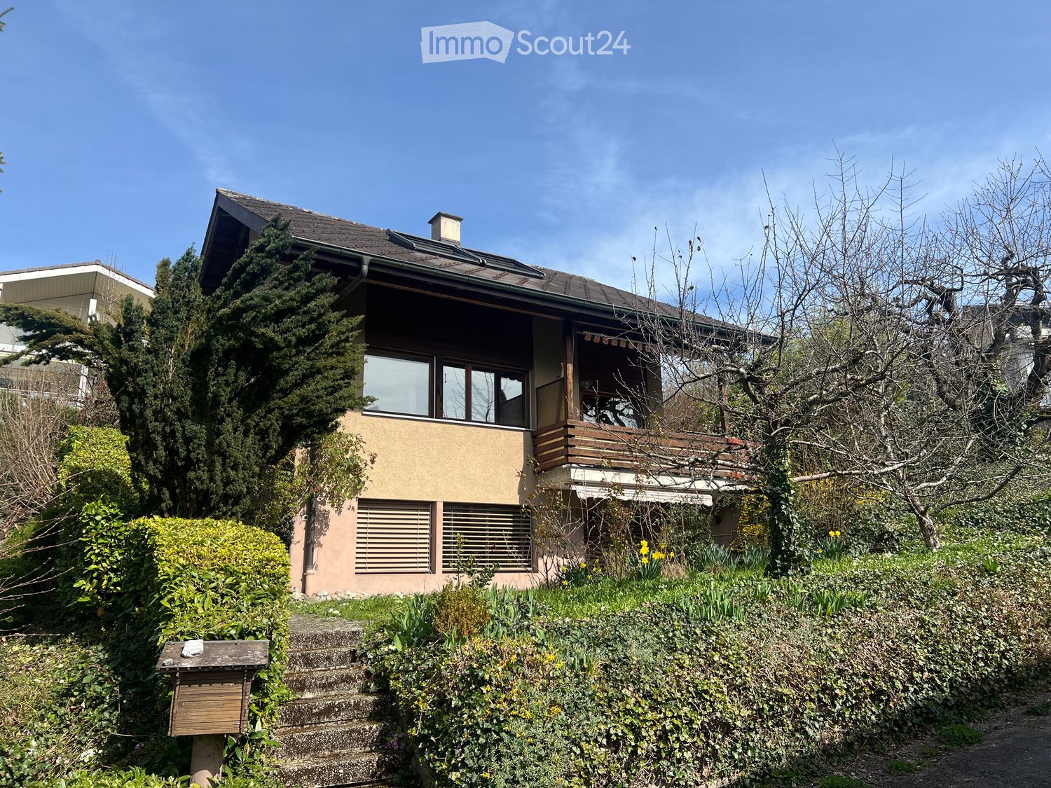 Two-story house with a modern design, featuring a balcony, large windows, and a well-maintained garden with steps leading up to the entrance.