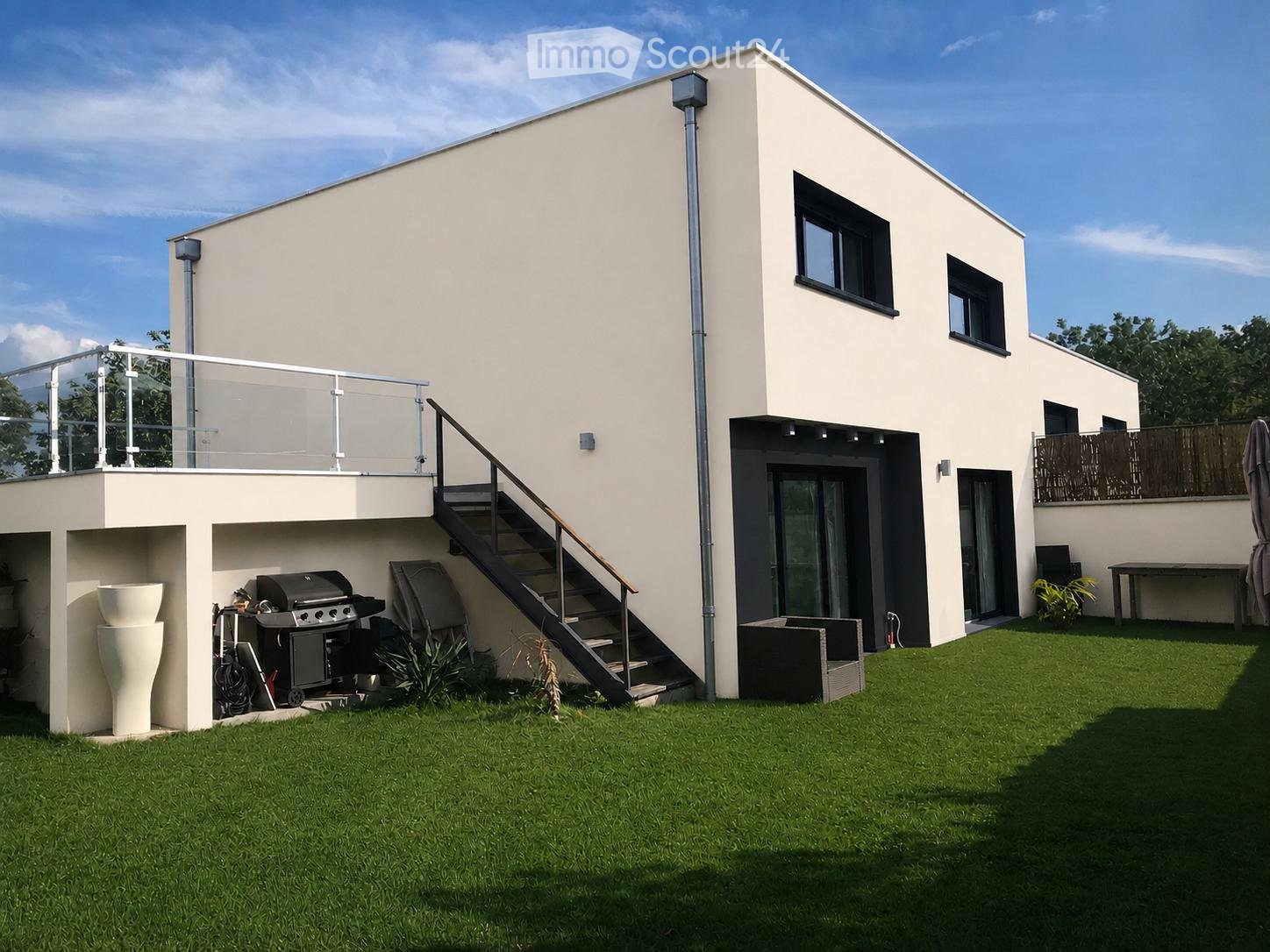 Modern two-story house with a raised ground floor, featuring a balcony, staircase, and outdoor grill area.
