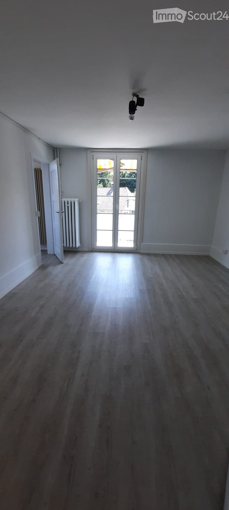 Empty room with wooden flooring, white walls, a sliding glass door leading outside, and a radiator on the left side.