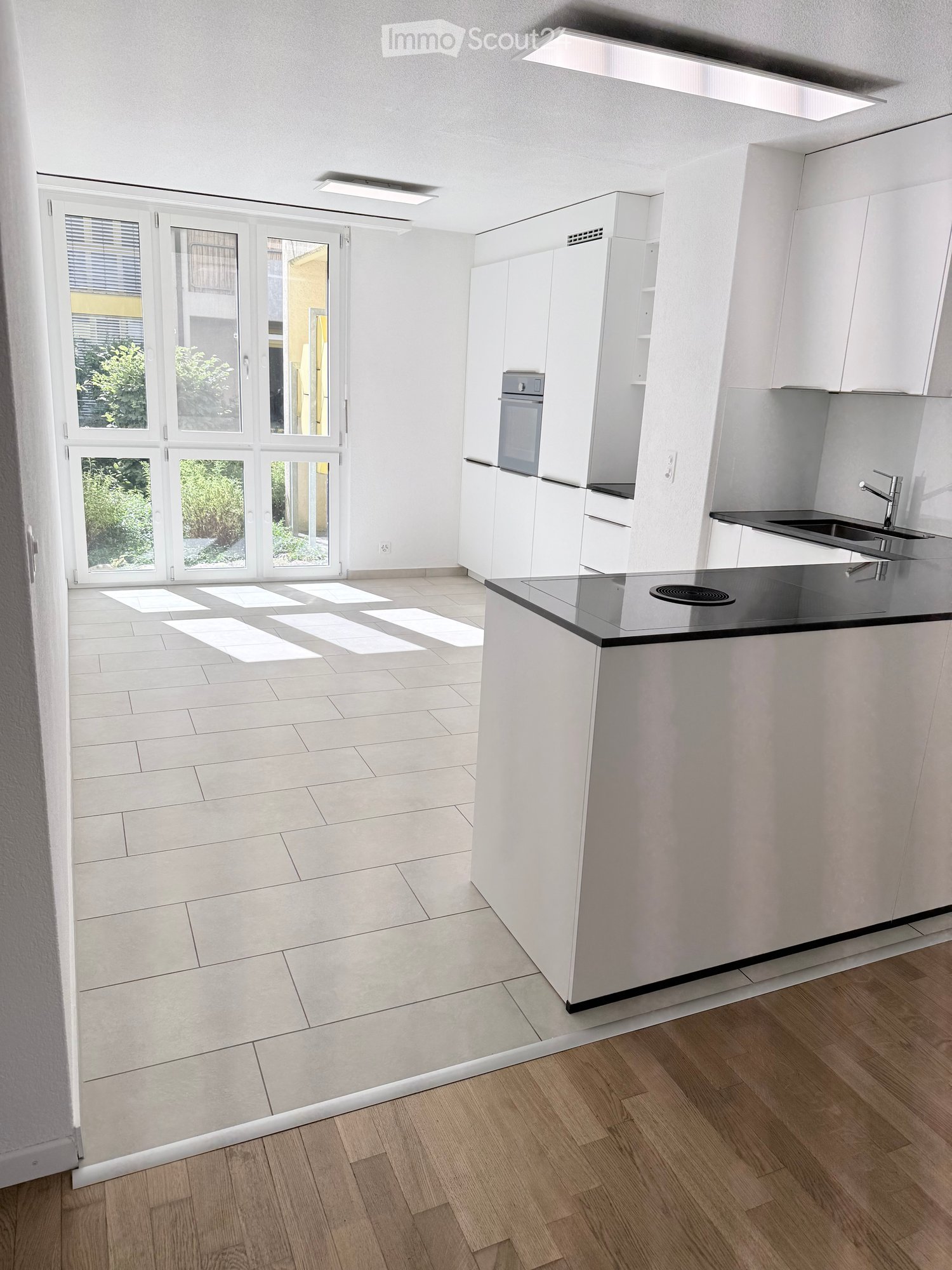 Modern kitchen with white cabinets, black countertop, and large windows. Features a sink, oven, and faucet.