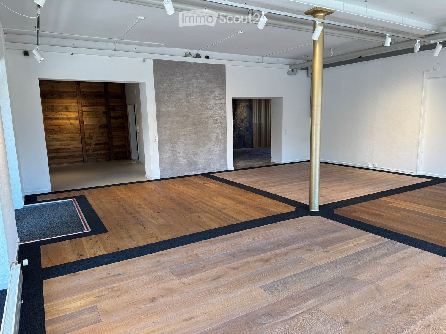 Empty room with wooden flooring, white walls, exposed ceiling beams, and a large wooden door in the background.