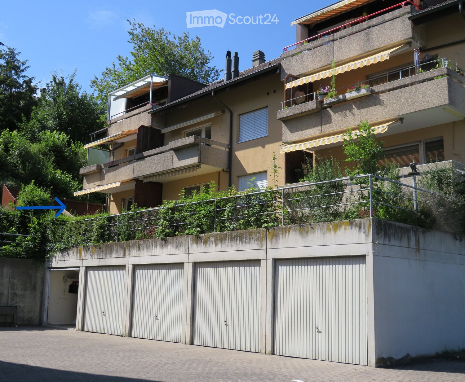 Multi-story residential building with balconies, awnings, and multiple garage doors at the base.