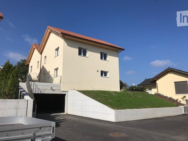 Two-story house with a raised ground floor, garage, and a small landscaped garden area.