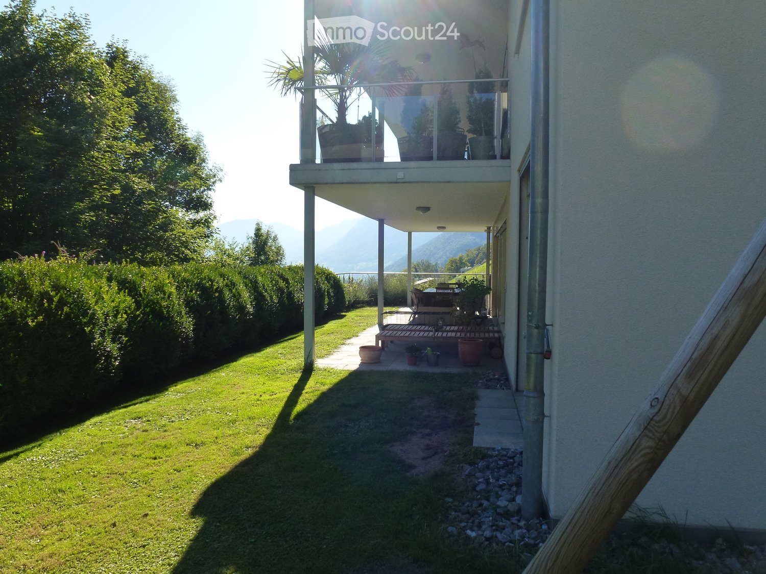Garden area with a well-maintained lawn, wooden deck, potted plants, and a covered balcony area with outdoor furniture.
