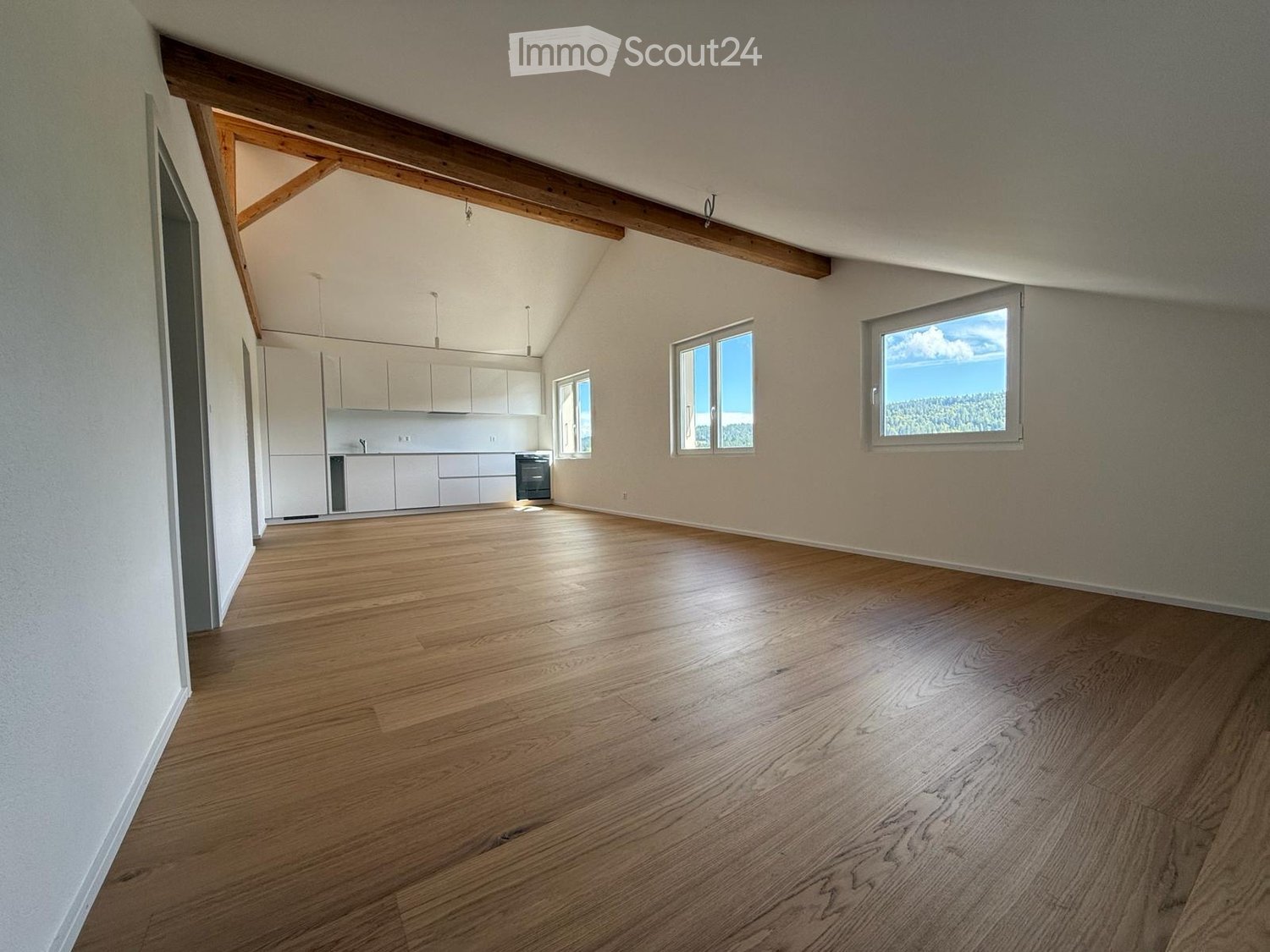 Empty room with wooden flooring, white cabinets, and large windows offering a scenic view.