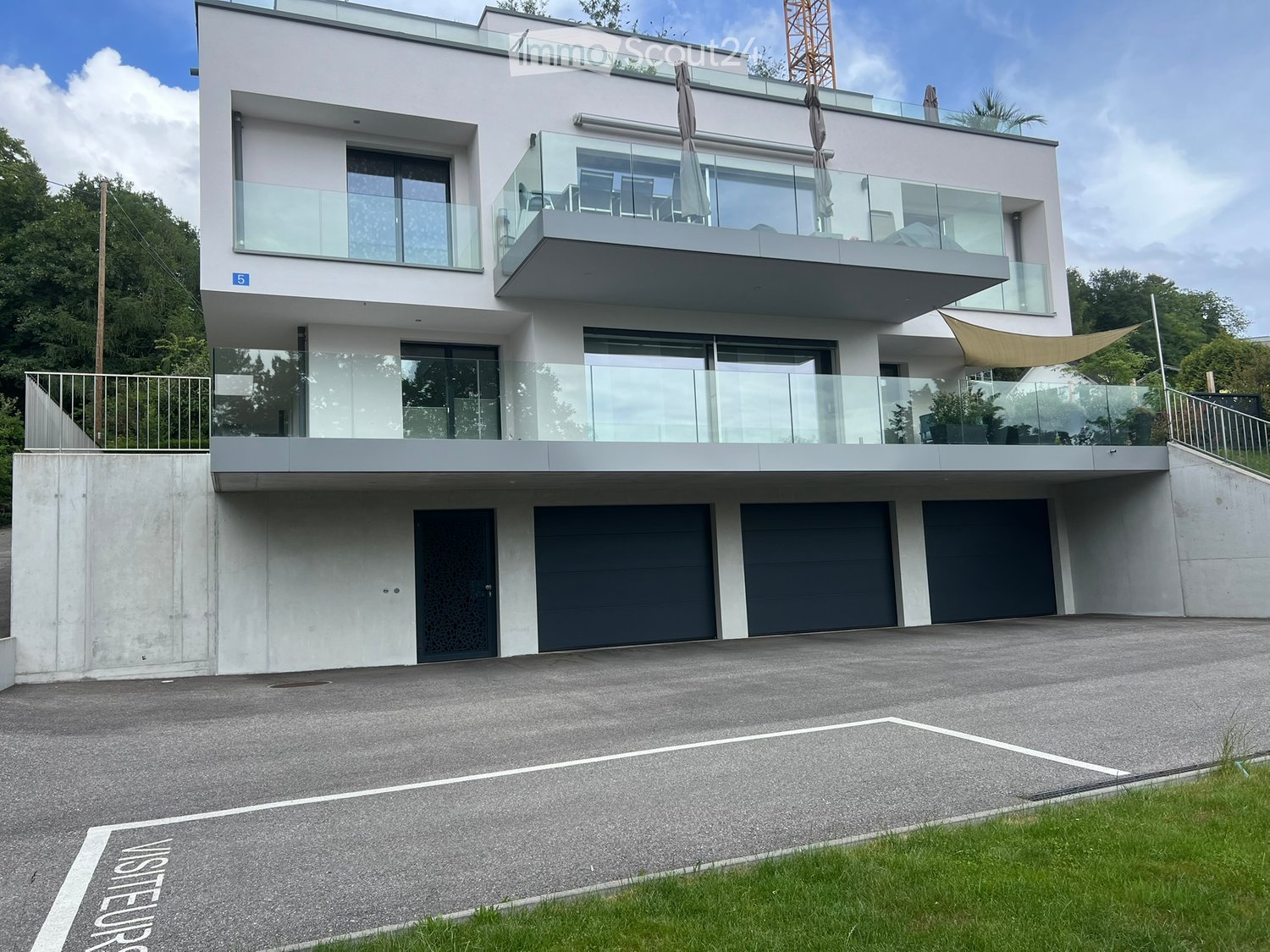 Modern two-story house with white facade, large glass balconies, and multiple garage doors.