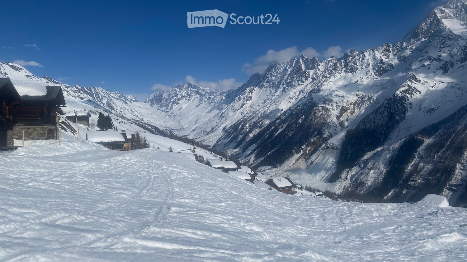 Snow-covered mountain landscape with scattered wooden chalets and cabins nestled among snow-covered slopes and peaks.