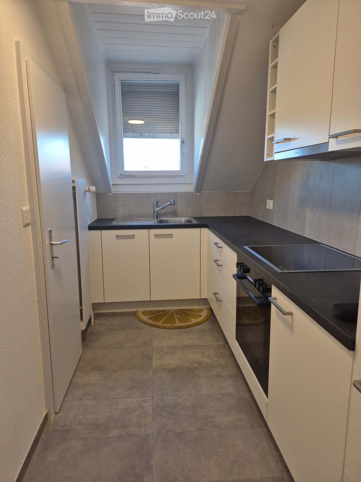 Modern kitchen with white cabinets, black countertops, stainless steel sink and faucet, stove, and oven. Features a window with blinds and a small rug on the floor.