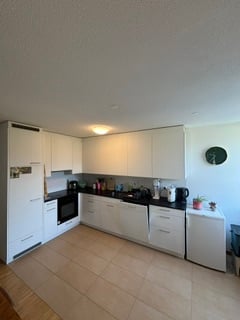 Modern kitchen with white cabinets, stainless steel appliances, and a central island. The space features a tiled floor and a sleek, contemporary design.