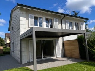 Modern two-story house with white exterior, large windows, covered patio, and garage.