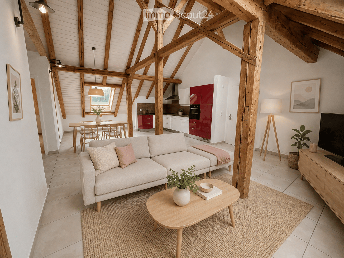 Open-plan living and dining area with exposed wooden beams, a grey sofa, coffee table, dining table with chairs, kitchen area with red cabinets, and a TV stand with a screen.