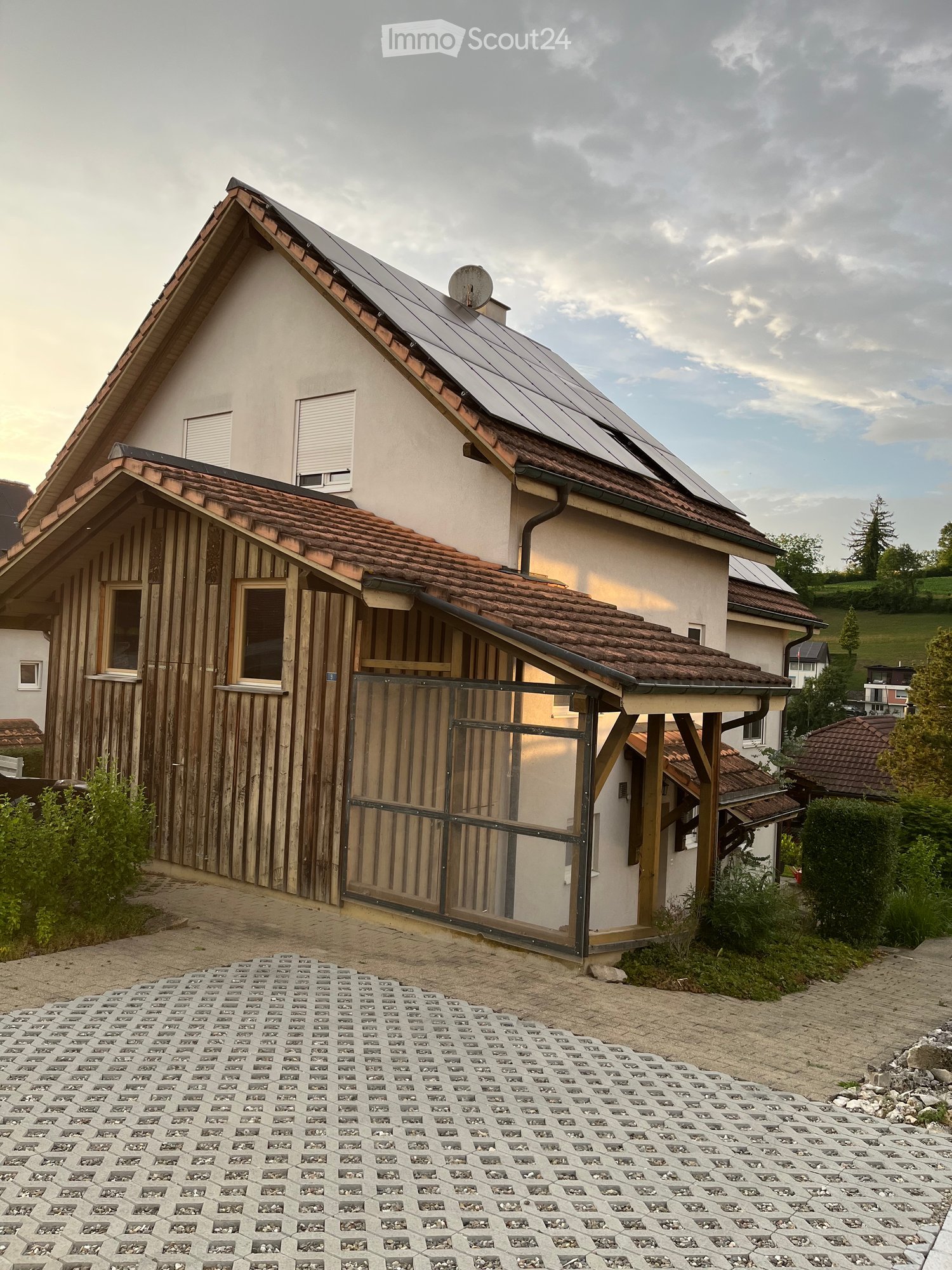 Two-story house with solar panels on the roof, wooden siding on one side, and a covered entrance area with a metal gate.