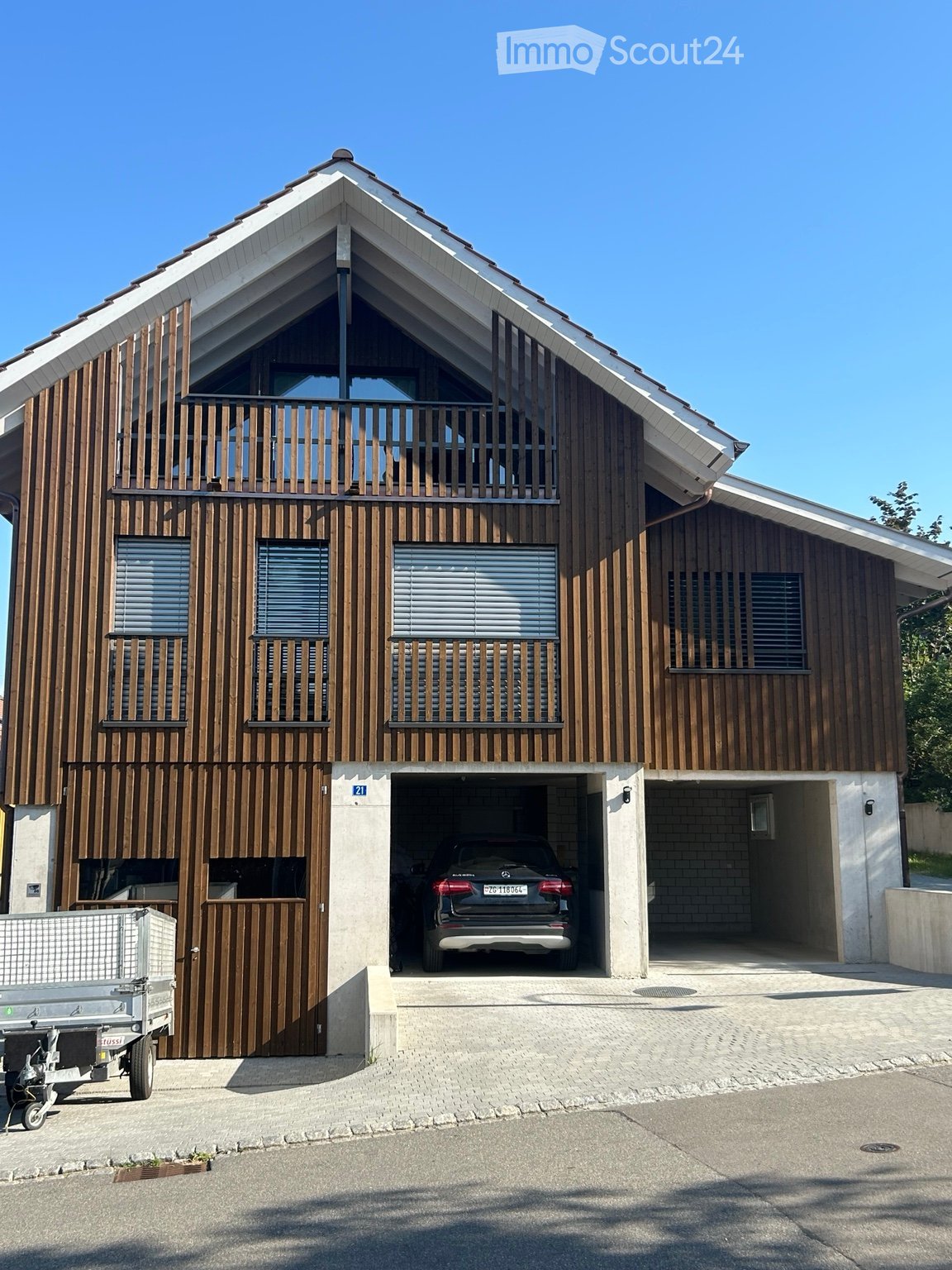 Modern two-story house with wooden facade, large garage, and balcony on the upper floor.